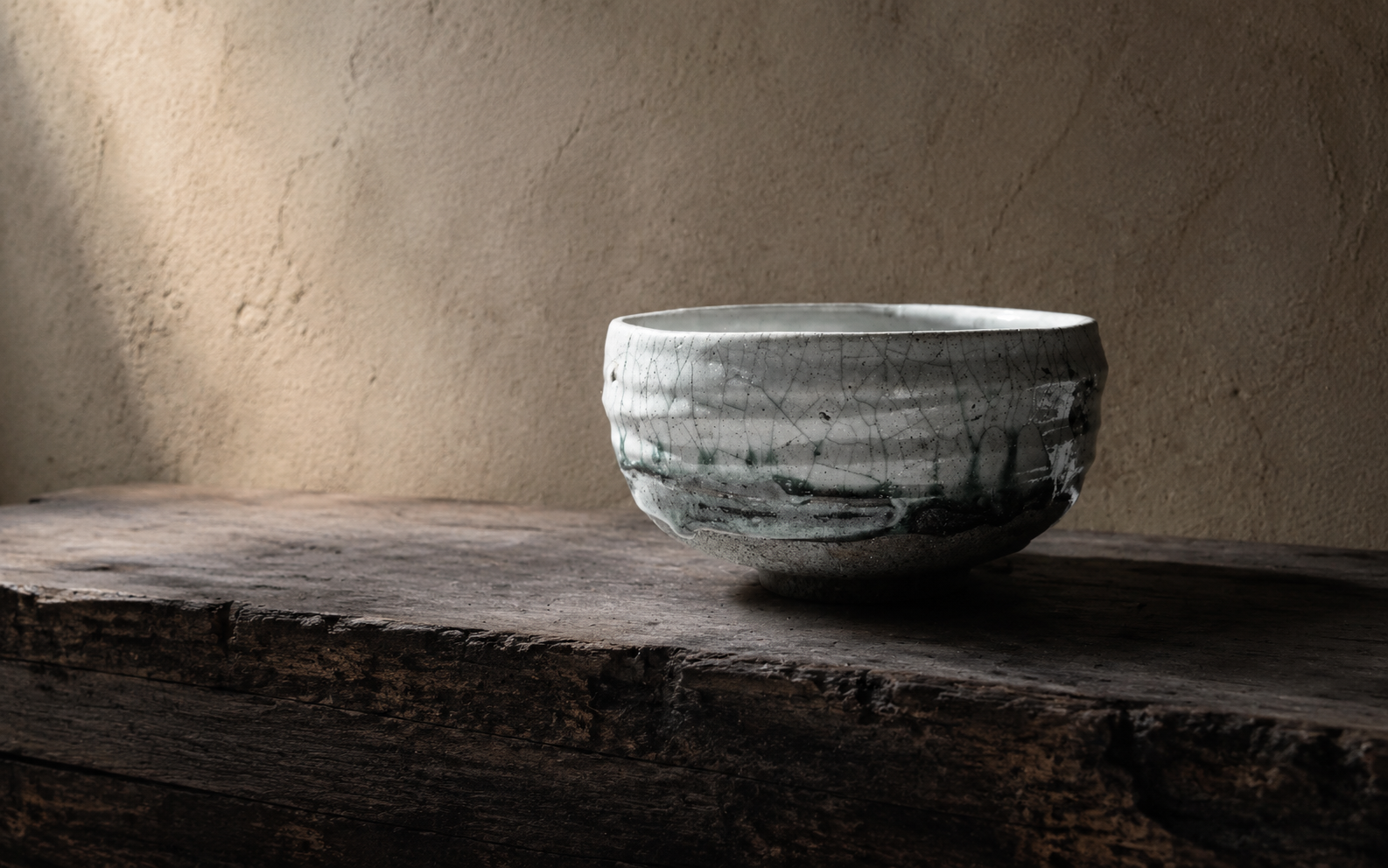 Textured clay wall, aged timber and a dark handmade ceramic bowl